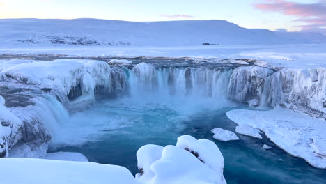 Fast-flowing-water-over-the-Godafoss-waterfalls-in-a-snowy-landscape-in-Iceland-after-sunset