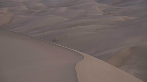 Panning-up-to-stunning-mountain-range-behind-sand-dune-field-at-sunrise