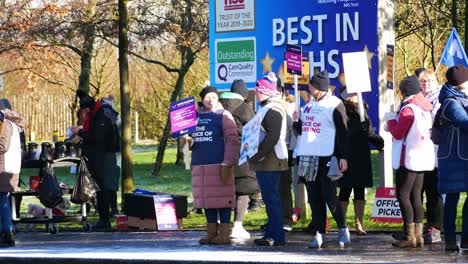 NHS-nurses-striking-for-fair-pay-and-better-care-outside-St-Helens-hospital-on-a-chilly-winter-morning,-waving-banners-and-flags
