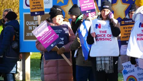NHS-nurses-strike-for-fair-pay,-waving-banners-and-flags-outside-cold-UK-hospital