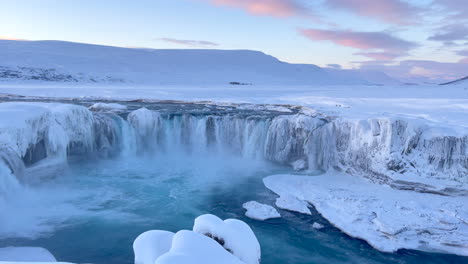 Water-crashes-down-the-wide-Godafoss-falls-into-a-snowy-landscape-just-after-sunrise