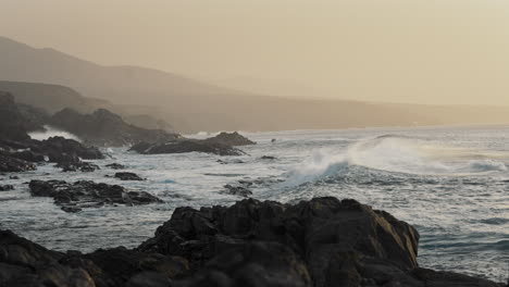 Rocky-ocean-shore-with-waves-splashing-on-rocks-and-orange-sky-in-the-background