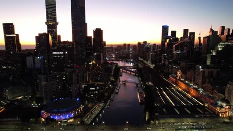 Aerial-flight-down-Yarra-river-Melbourne-with-golden-sunset-city-lights