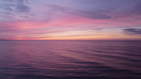 Drohnenaufstieg-über-Einem-Ruhigen-Meer,-über-Dem-Die-Sonne-In-Einem-Magischen-Sonnenuntergang-In-Intensiven-Pastellfarben-Untergeht