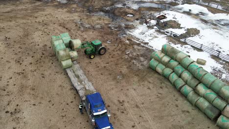 Aerial-View-of-Tractor-Unloading-Round-Bales-from-a-Flatdeck-Semi-Truck-on-a-Farm-in-British-Columbia,-Canada