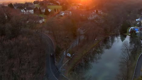 Jeep-Auto,-Das-Im-Winter-Die-Kurvenreiche-Straße-Neben-Dem-Malerischen-See-Hinauffährt,-Mit-Goldenem-Sonnenlicht-Vom-Sonnenuntergang