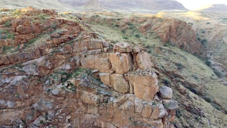 Vista-Aérea-Cinematográfica-Rodeando-Rocas-Besándose-En-Una-Exuberante-Garganta-Del-Desierto-Entre-Acantilados-A-La-Hora-Dorada-En-El-Parque-Riemvasmaak-En-Sudáfrica-Cerca-De-Namibia