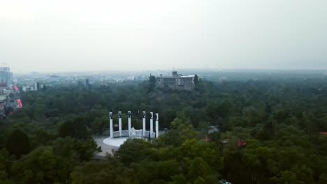 Tilt-down-aerial-orbit-with-Chapultepec-Castle-and-the-"Altar-a-la-Patria"-on-a-cloudy-and-mysterious-day-over-Chapultepec-Forest,-the-most-beautiful-park-in-the-world,-Mexico-City