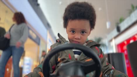 Surprised-two-year-old-black-baby,-mix-raced,-driving-a-remote-controlled-toy-car-inside-a-Mall