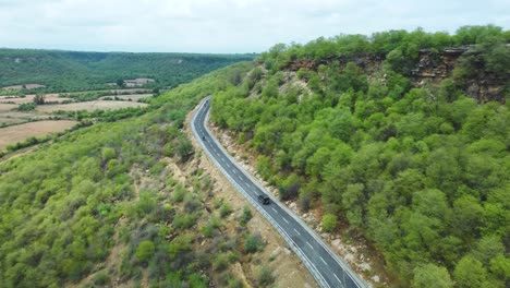 Aerial-drone-view-of-a-car-and-motorcycle-driving-on-a-curved-country-road-in-the-hills