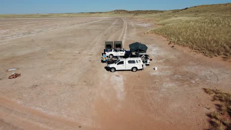 Filmische-Luftaufnahme-über-Autos-Mit-Dachzelten-In-Einer-Salzpfanne-In-Der-Sonnigen-Kalahari-wüstenlandschaft-In-Südafrika-In-Der-Nähe-Von-Namibia