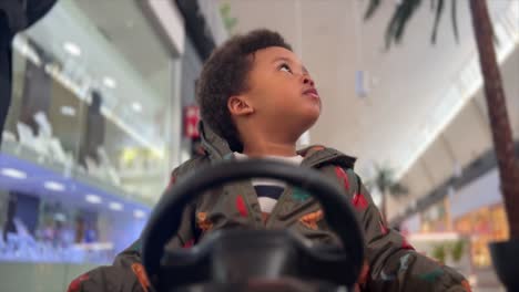 Exotic-and-cute-two-year-old-black-baby-drives-a-big-toy-car-inside-a-mall