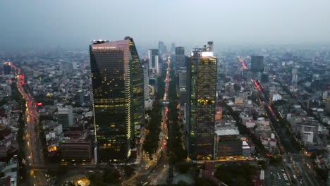 Dolly-in-aerial-view-of-the-BBVA-Tower-and-Torre-Mayor-on-Paseo-de-la-Reforma-Avenue-at-night-with-car-lights-and-illuminated-architecture,-Mexico-City