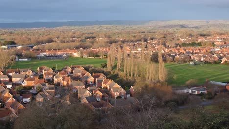 Panoramic-landscape-view-of-Glastonbury-town-in-Somerset,-England,-with-red-brick-houses-on-housing-estate,-green-football-fields-and-church-spires
