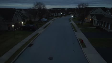 Aerial-flight-over-dark-street-at-night-in-American-residential-neighborhood-lit-by-street-lights