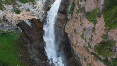 Aerial-shot-Barskoon-Waterfall-in-Fairy-Tale-Canyon-in-Kyrgyzstan,-starting-downward-and-then-tilting-to-reveal-falls,-drone-footage