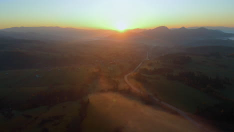 Aerial-shot-of-polish-ountryside-with-hills-and-fields-covered-in-morning-mist-with-yellow-sunrise-and-orange-sky