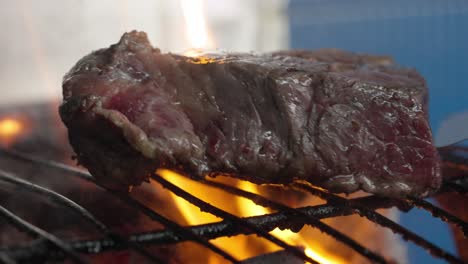 A-cook-turns-a-rare-steak-on-a-barbecue-with-embers-and-flames