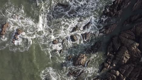 Aerial-drone-bird's-eye-view-of-waves-crashing-over-a-rocky-coastline---Lee-Bay,-Beach,-Ilfracombe,-Devon,-England