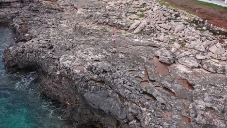 Aerial-view-of-person-walking-along-rocky-shoreline-in-Spain