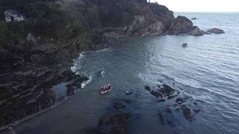 Aerial-drone-tracking-shot-of-people-on-a-multi-person-paddleboard,-paddling-out-to-sea-from-the-beach---Lee-Bay,-Beach,-Ilfracombe,-Devon,-England