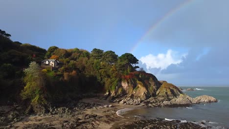 Aerial-drone-tracking-shot-of-an-English-beach-with-rocky-cliffs-and-a-rainbow-in-the-background---Lee-Bay,-Beach,-Ilfracombe,-Devon