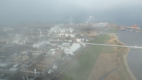 Smoke-and-steam-rising-of-an-industrial-facility-on-a-river,-CO2-emissions,-air-pollution,-exhaust-gases,-aerial,-flight-through-steam