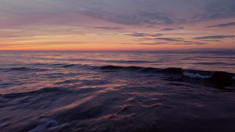 Niedrige-Luftdrohne,-Die-über-Meerwasserwellen-Am-Auffälligen-Orangefarbenen-Sonnenuntergangshimmel-Fliegt