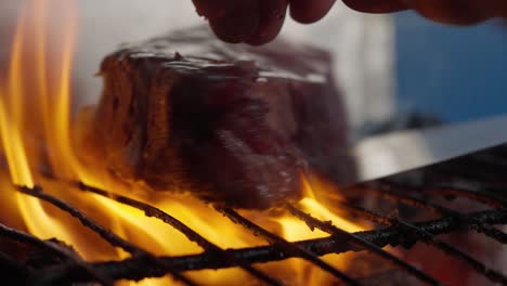 A-cook-turns-a-grilled-steak-amid-flames,-smoke-and-barbecue-coals