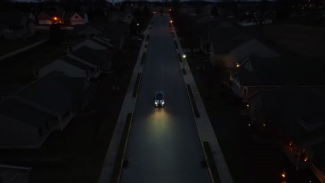 Aerial-view-of-car-driving-through-dark-American-neighborhood-at-night