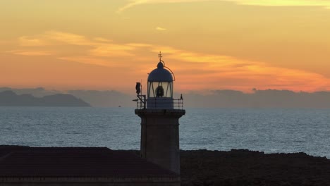 Aerial-long-zoom-orbit-around-Punta-Nati-Lighthouse-during-golden-hour-sunset-in-Menorca,-Spain