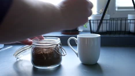 A-man-putting-coffee-granules-into-a-cup-with-a-spoon-in-a-kitchen