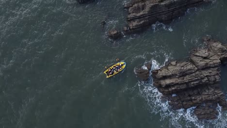 Aerial-drone-bird's-eye-view-of-people-on-a-yellow-multi-person-paddleboard-navigating-rocks-along-the-coastline-under-a-rocky-cliff-face---Lee-Bay,-Beach,-Ilfracombe,-Devon,-England