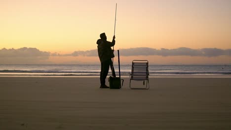 Tiefwinkelaufnahme-Eines-Fischers,-Der-Bei-Sonnenaufgang-Seinen-Angelstock-Am-Magischen-Sandstrand-Befestigt
