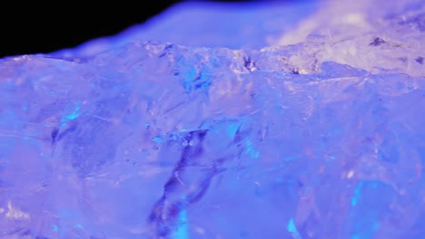 Crystal-clear-quartz-illuminated-by-cool-ice-purple-light-on-dark-background,-captured-through-smooth-panning-and-macro-lens