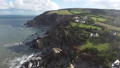 Aerial-drone-orbit-shot-of-coastal-village-on-top-of-a-cliff-with-waves-crashing-on-rock-formations-below---Lee-Bay,-Beach,-Ilfracombe,-Devon