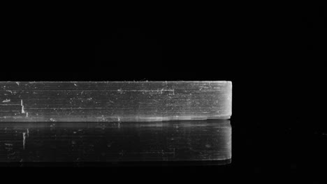 Side-view-of-clear,-transparent-selenite-shard-as-it-pans-across-a-black-background,-studio-lit-for-maximum-clarity