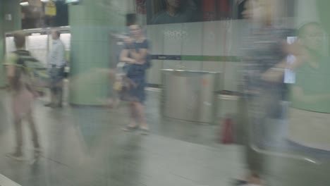 POV-from-inside-a-subway-arriving-at-a-green-subwaystation-in-Munich,-Germany,-while-people-are-waiting-for-it-to-arrive