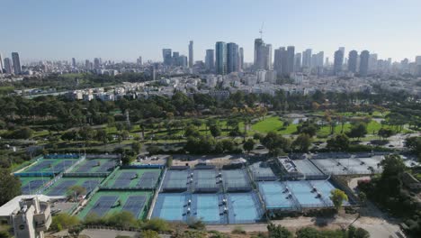 Statische-Aufnahme-über-Tennisplätzen-Mit-Einem-Malerischen-Stadtbild-Eines-Parks-Und-Eines-Flusses-In-Der-Nähe-Von-Wohntürmen