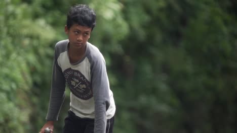 Slow-motion-shot-of-an-Indonesian-young-boy-riding-his-bicycle-looking-directly-into-camera,-Bali