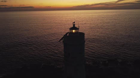 Stunning-aerial-drone-view-of-Lighthouse-flashes-with-seagul-on-head-top,-sunset