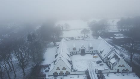 Drohne,-Die-Im-Winter-Von-Einem-Wunderschönen,-Schneebedeckten-Alten-Bauernhof-Im-Ländlichen-Holland-Wegfliegt