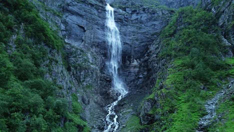 Filmische-Drohnenaufnahme-Eines-Gigantischen-Wasserfalls,-Der-In-Der-Abenddämmerung-Zwischen-Grünen-Bergen-Plätschert