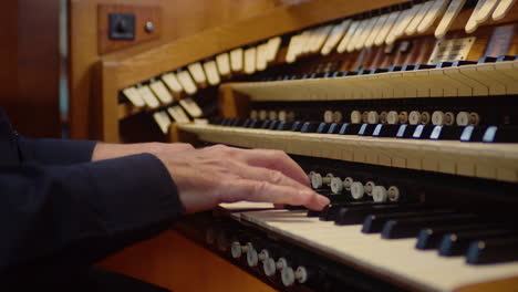 Close-up-man-plays-pipe-organ-keyboard-wearing-black-suit-in-a-church