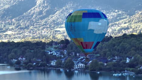 Hot-air-balloon-descending-down-by-a-lake-in-a-summer-morning-in-Annecy,-France