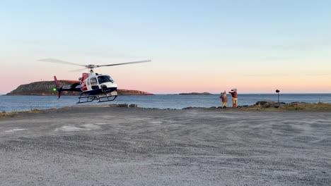 Medium-shot-of-a-helicopter-taking-off-near-a-body-of-water-during-sunset-with-a-rocky-island-in-the-background