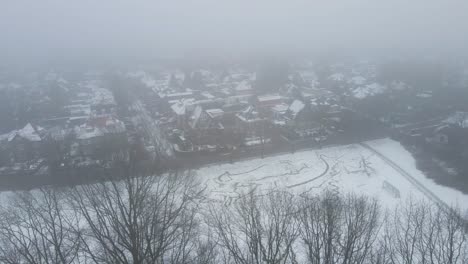 Drone-flying-over-trees-in-winter-towards-a-wealthy-suburban-neighborhood-hidden-in-fog