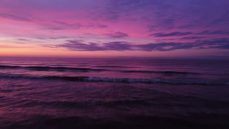 Backward-drone-flight-over-a-calm-sea-under-a-spectacular-pink-and-purple-sunrise
