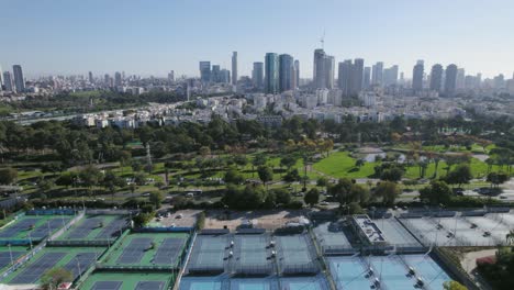 slow-flight-over-tennis-courts-with-a-picturesque-cityscape-of-a-park-and-river-near-residential-towers
