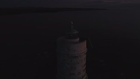 Cinematic-aerial-shot-of-Lighthouse-light-flashing,-seagull-bird-on-top,-dusk